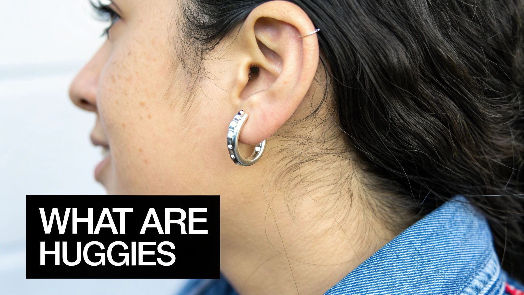 A person wearing several small huggie hoop earrings stacked on their earlobe