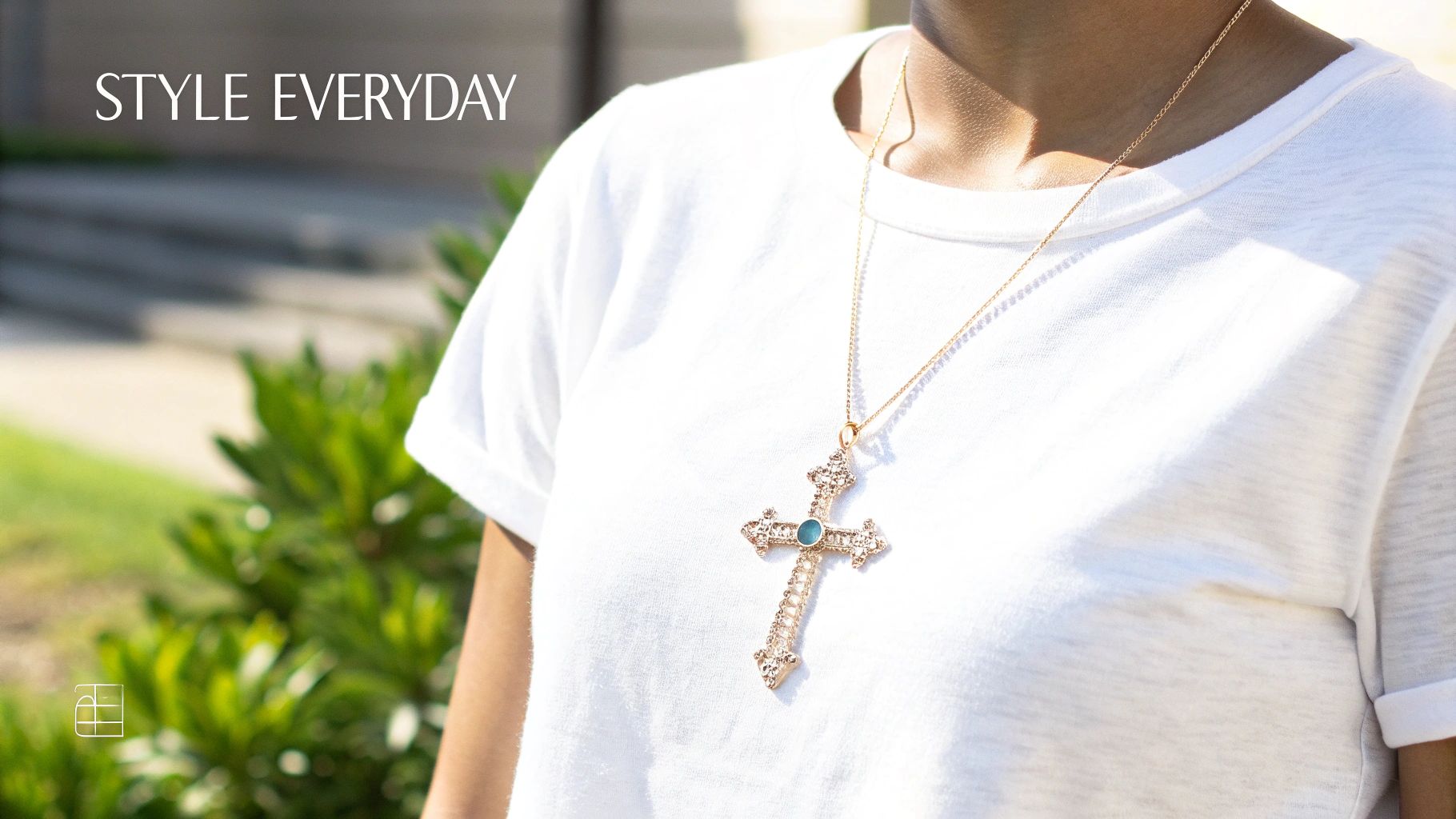 Close-up of a person wearing a white t-shirt and a decorative golden cross pendant with a turquoise gem.