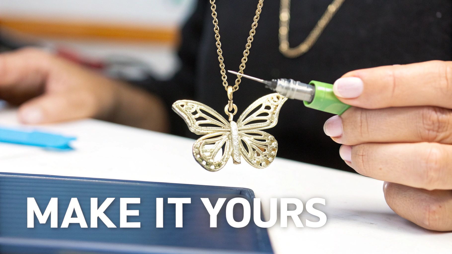 A person uses a precise tool to refine a beautiful gold butterfly pendant on a delicate chain.