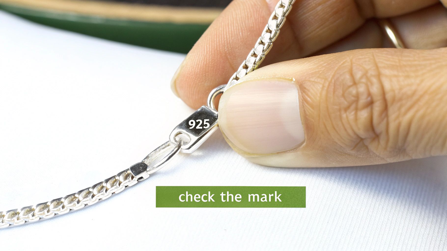 Close-up of a hand holding a sterling silver chain necklace with a '925' mark on its clasp.