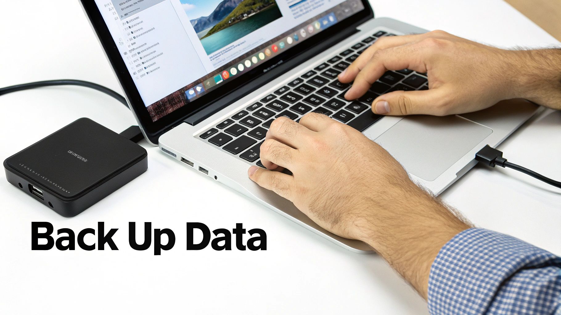 Close-up of hands typing on a laptop, connected to an external hard drive for data backup.
