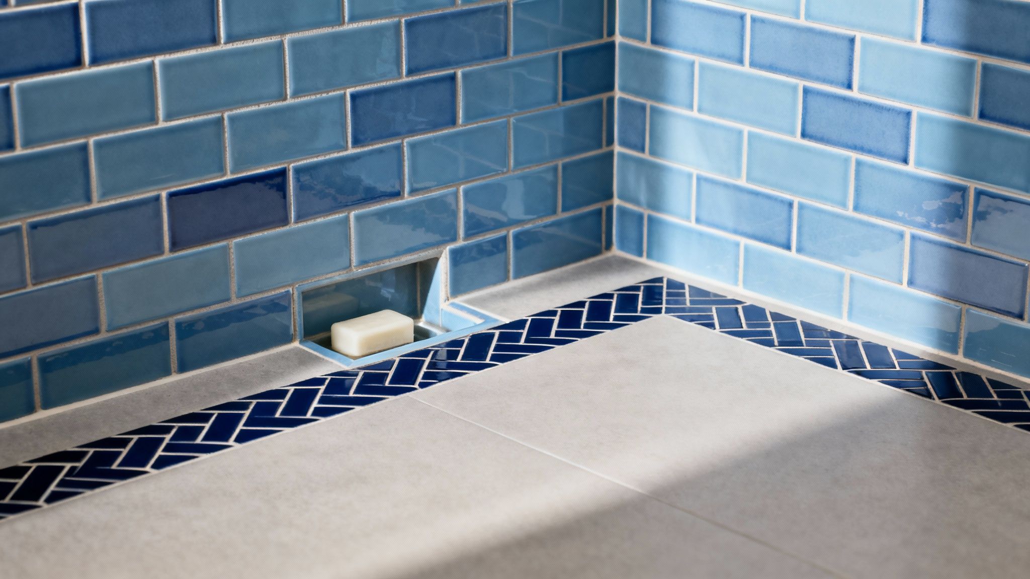 Close-up of a modern bathroom corner featuring blue subway tiles and a built-in soap niche.