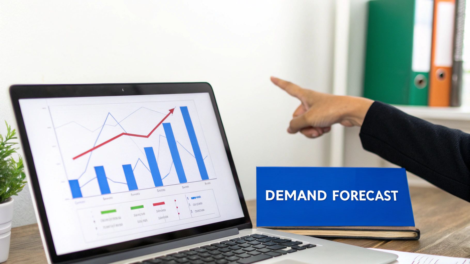 A hand points to a laptop screen displaying a demand forecast chart with an upward trend, next to a blue folder.