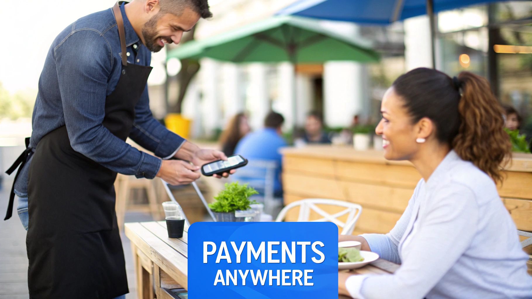 A smiling waiter processes a mobile payment for a happy female customer at an outdoor cafe.