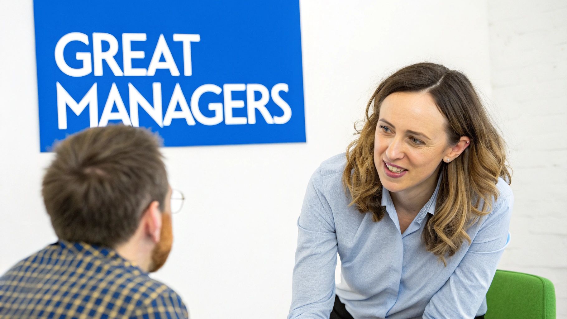 A smiling woman in a blue shirt talks to a man, with a 'GREAT MANAGERS' sign in the background.