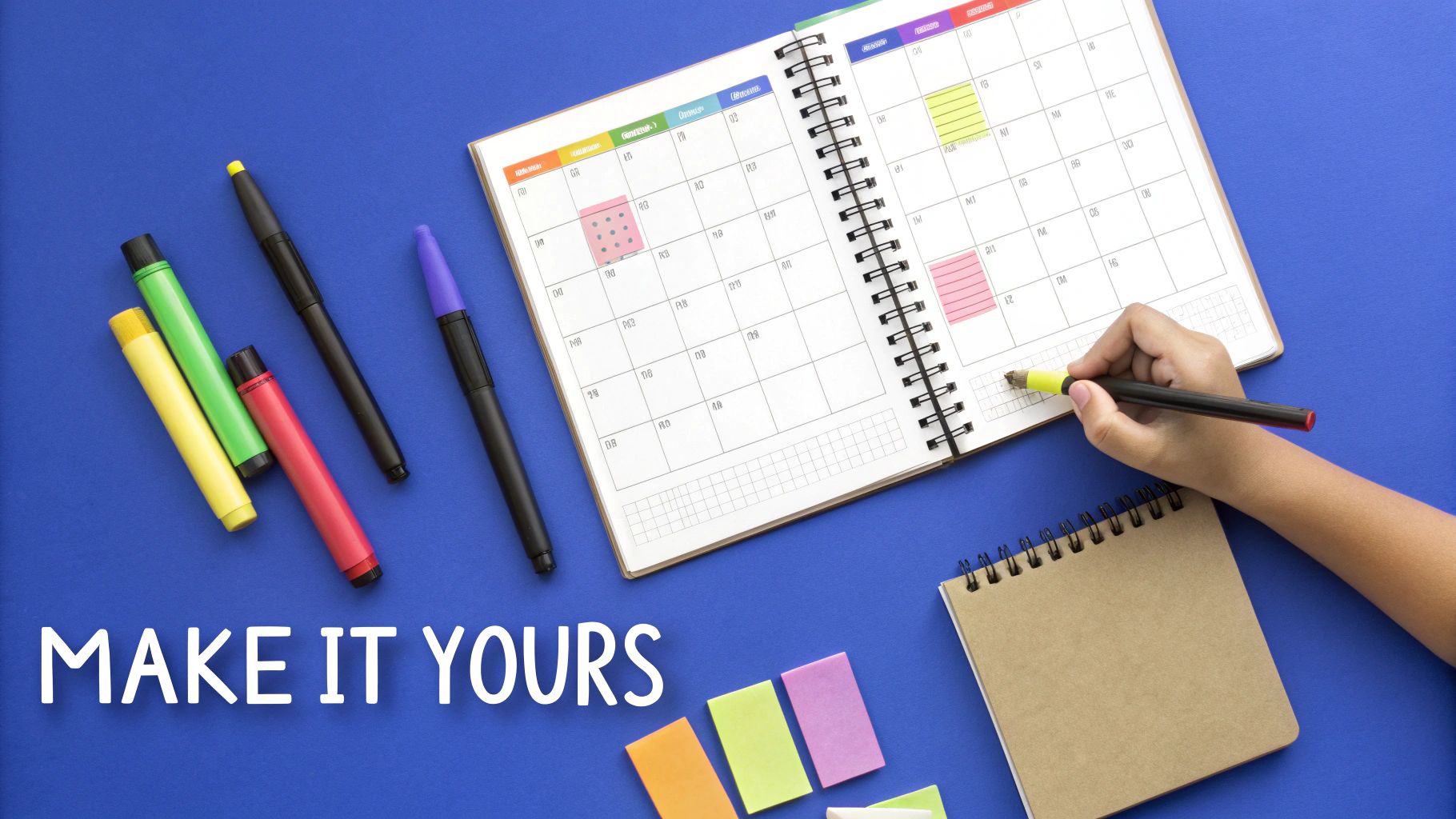 Overhead view of a hand highlighting a planner on a blue desk with colorful pens and sticky notes.