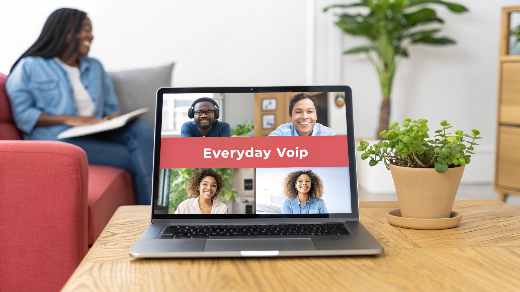 Laptop on a wooden table displays an 'Everyday Voip' video call with four smiling people, while a woman reads on a red sofa.