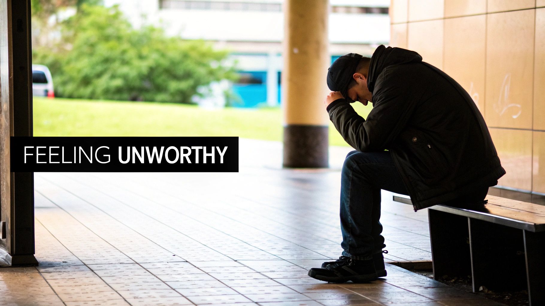 A man sits alone on a bench, head bowed in despair, feeling unworthy.