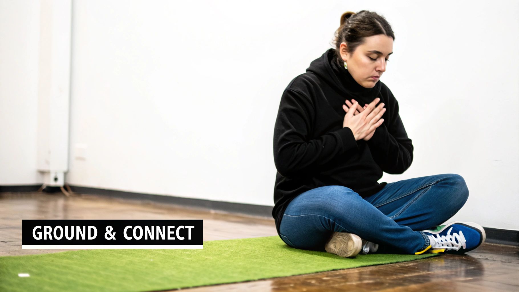 A woman meditates on a green mat, hands clasped over her chest, eyes closed for focus and connection.