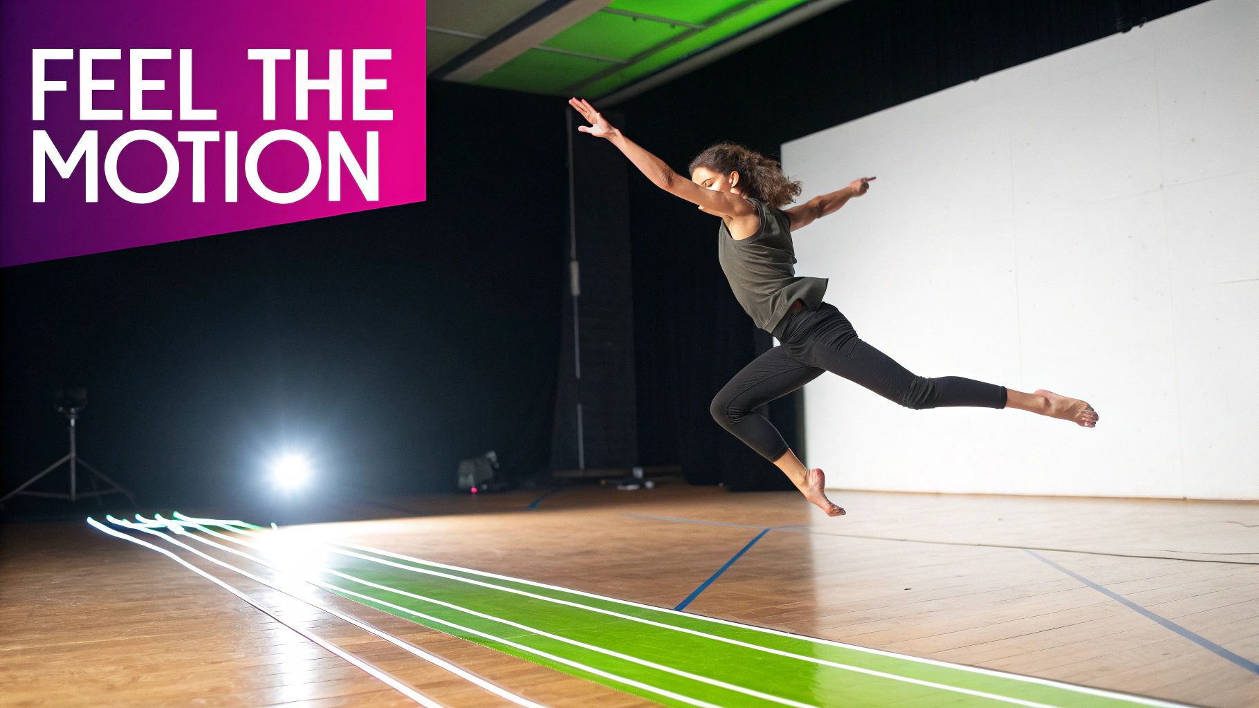 A dancer leaps gracefully over bright green illuminated lines on a wooden floor in a studio.