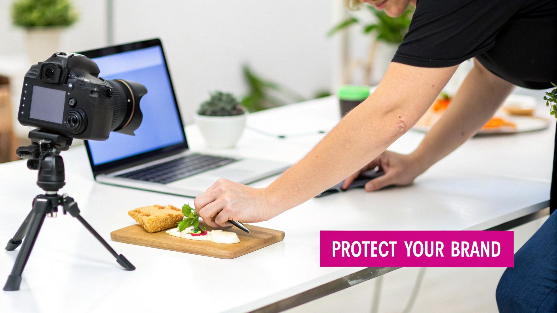 Close-up of a person styling food on a wooden board, with a camera and laptop in the background.