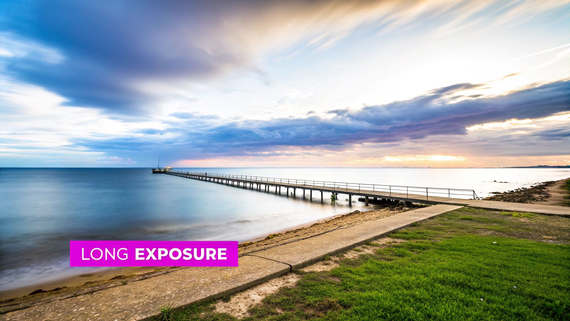 Long exposure photography of pier extending into calm ocean water at sunset