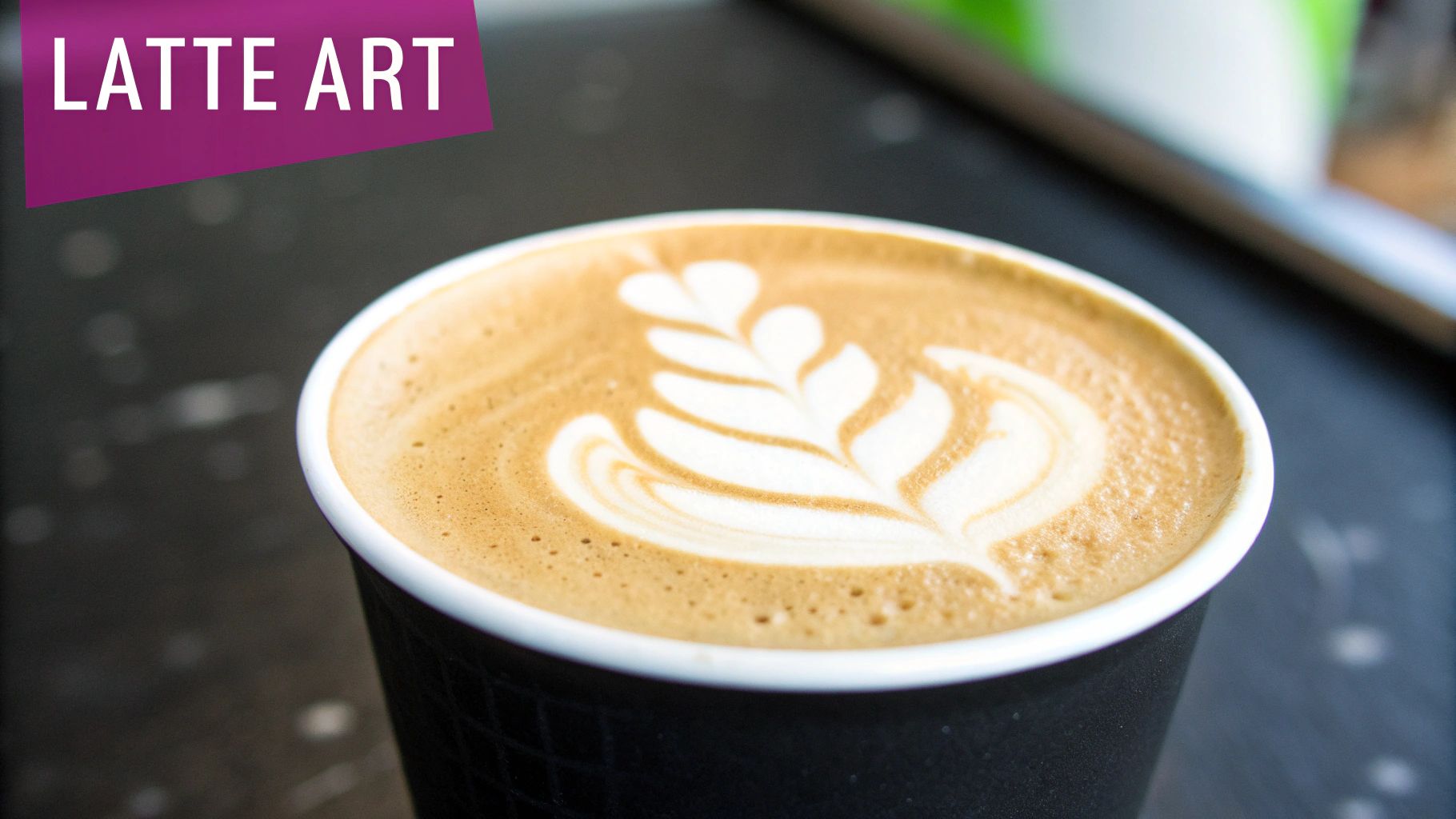 A close-up of a black coffee cup with beautiful leaf-shaped latte art on a dark surface.