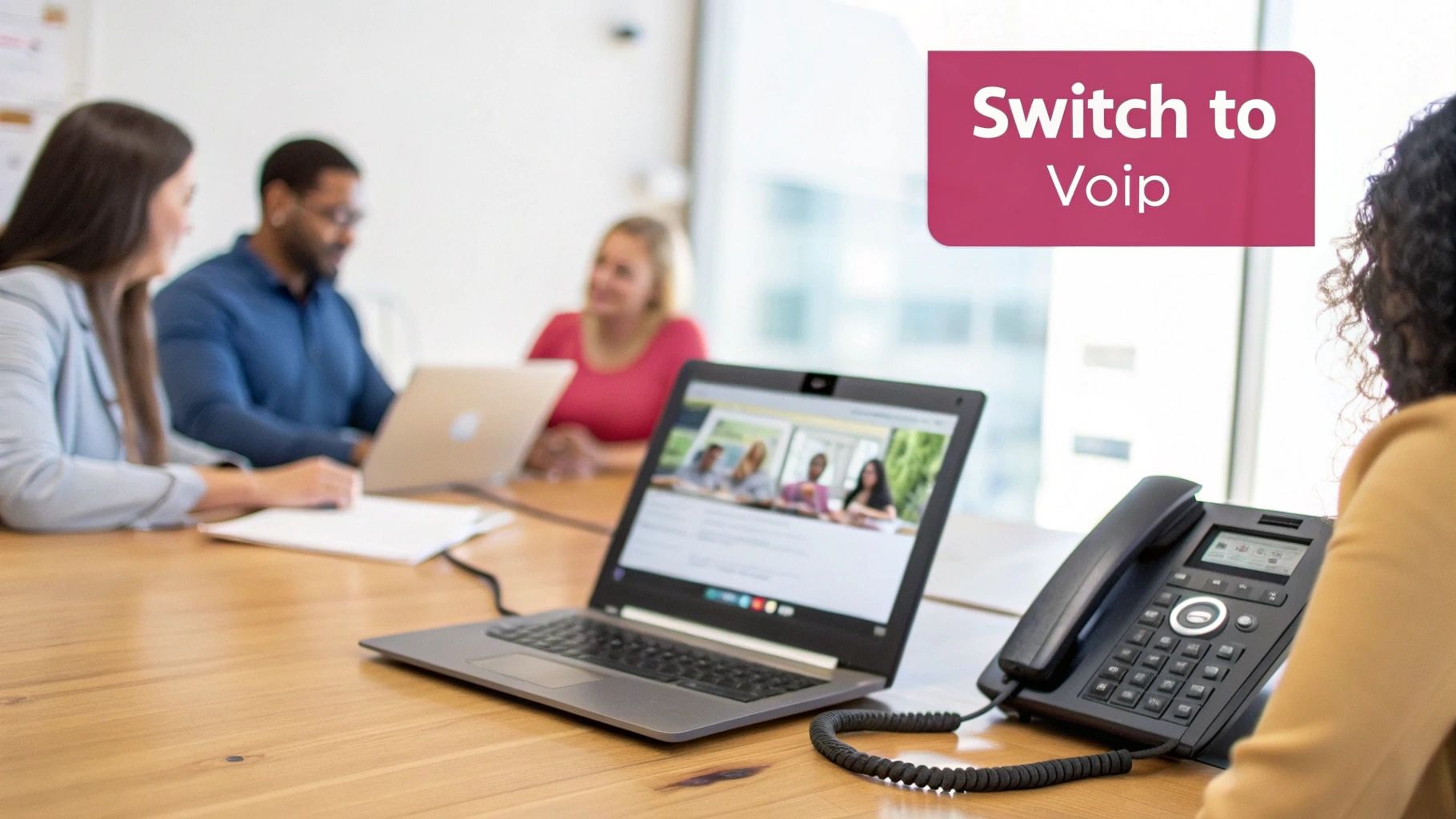 Uk Guide To Voice Over Ip Office Phone Systems Diverse Group In Office Meeting, Laptop Showing Video Call, And Voip Desk Phone.