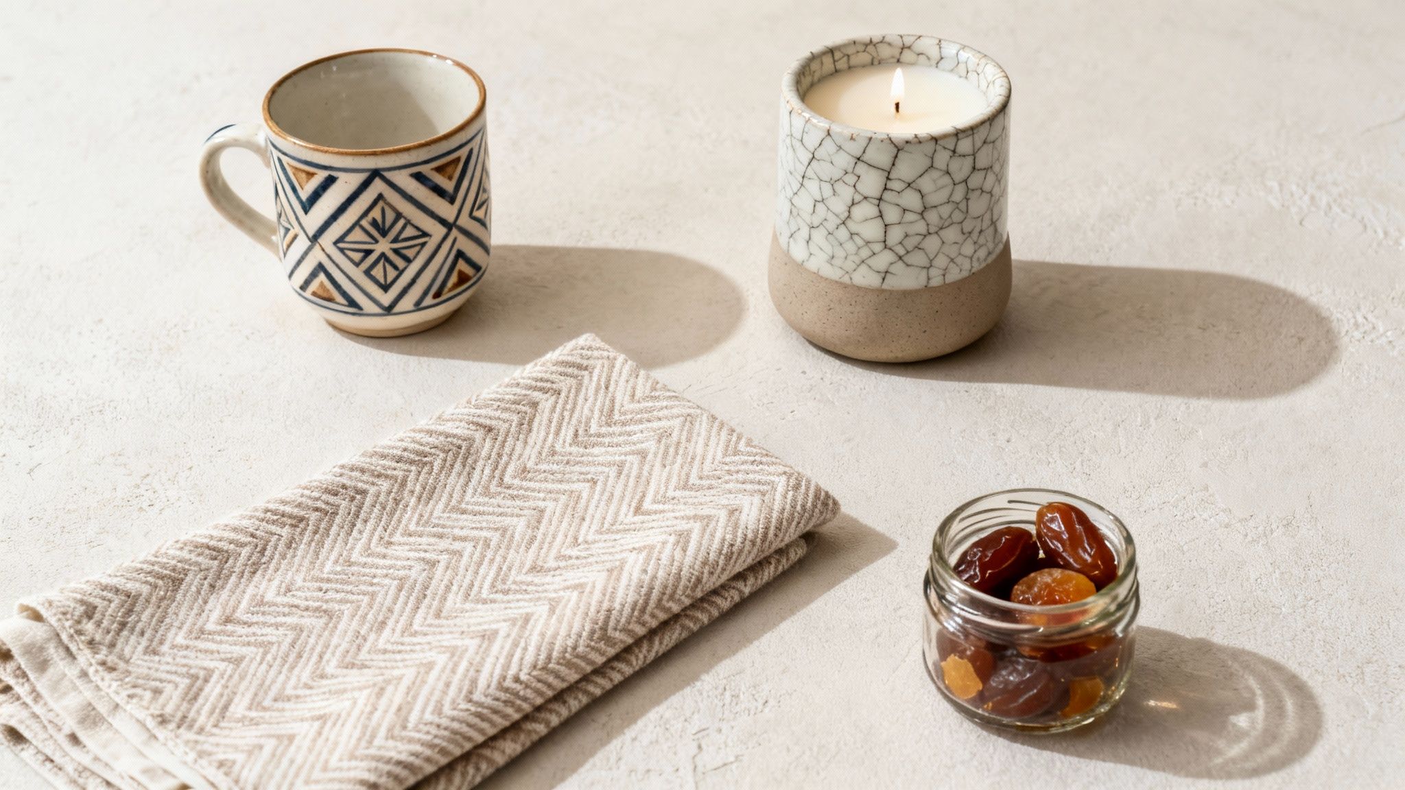 A minimalist setup featuring a patterned mug, a lit candle, a folded napkin, and dates in a jar.