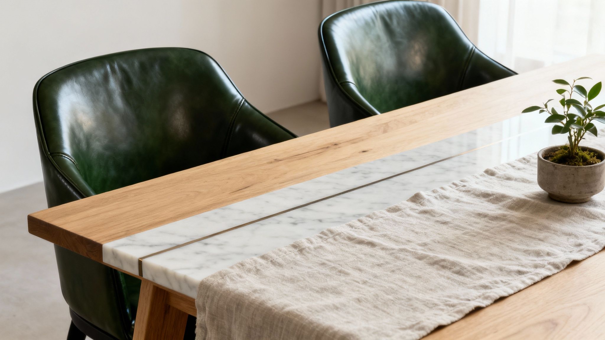 Two green leather dining chairs flank a modern dining table with wood, marble, and a linen runner.