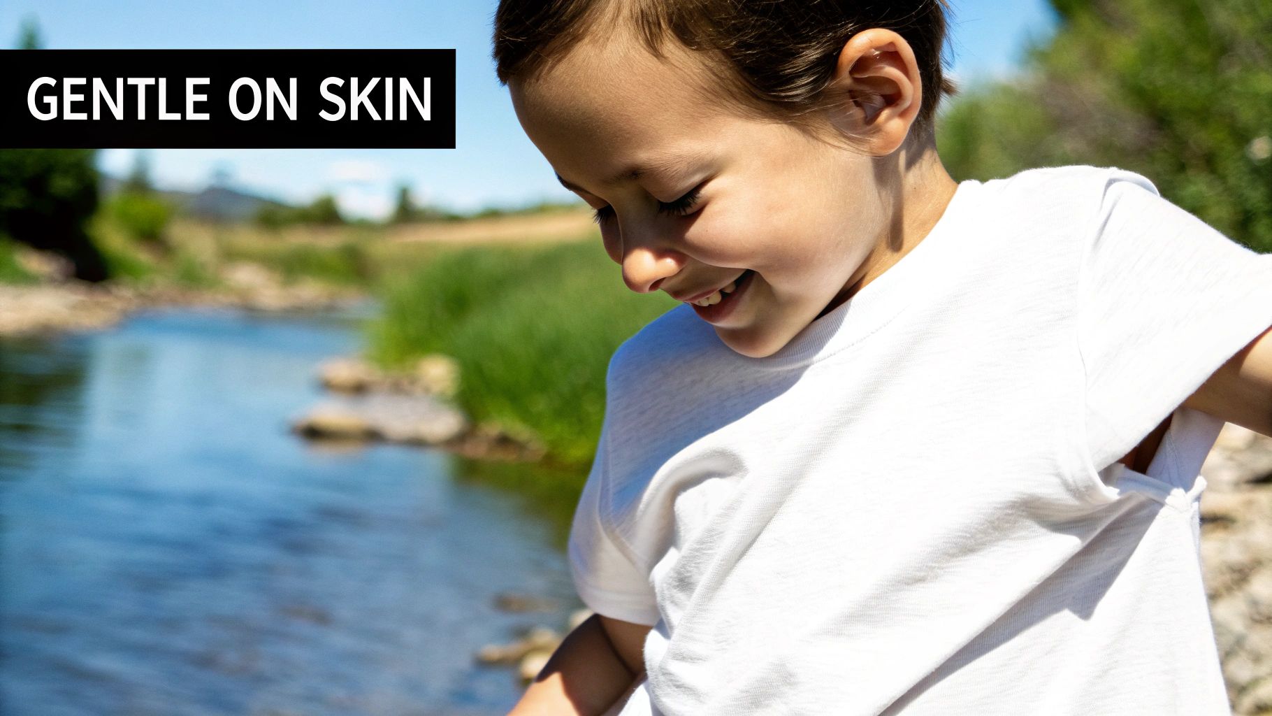 A happy child wearing a white t-shirt outdoors by a river, with 'GENTLE ON SKIN' text.