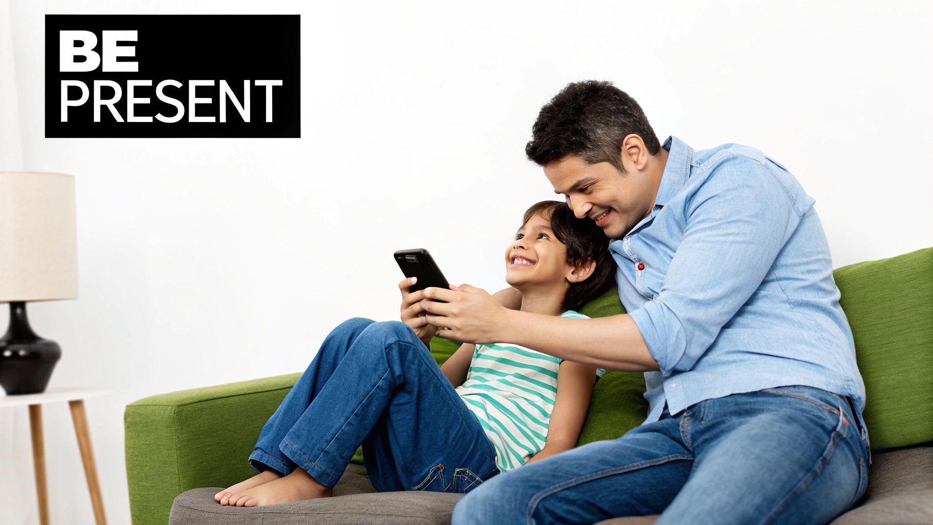 A father and child share a mindful moment on a couch, focused on a smartphone, with a 'BE PRESENT' sign.