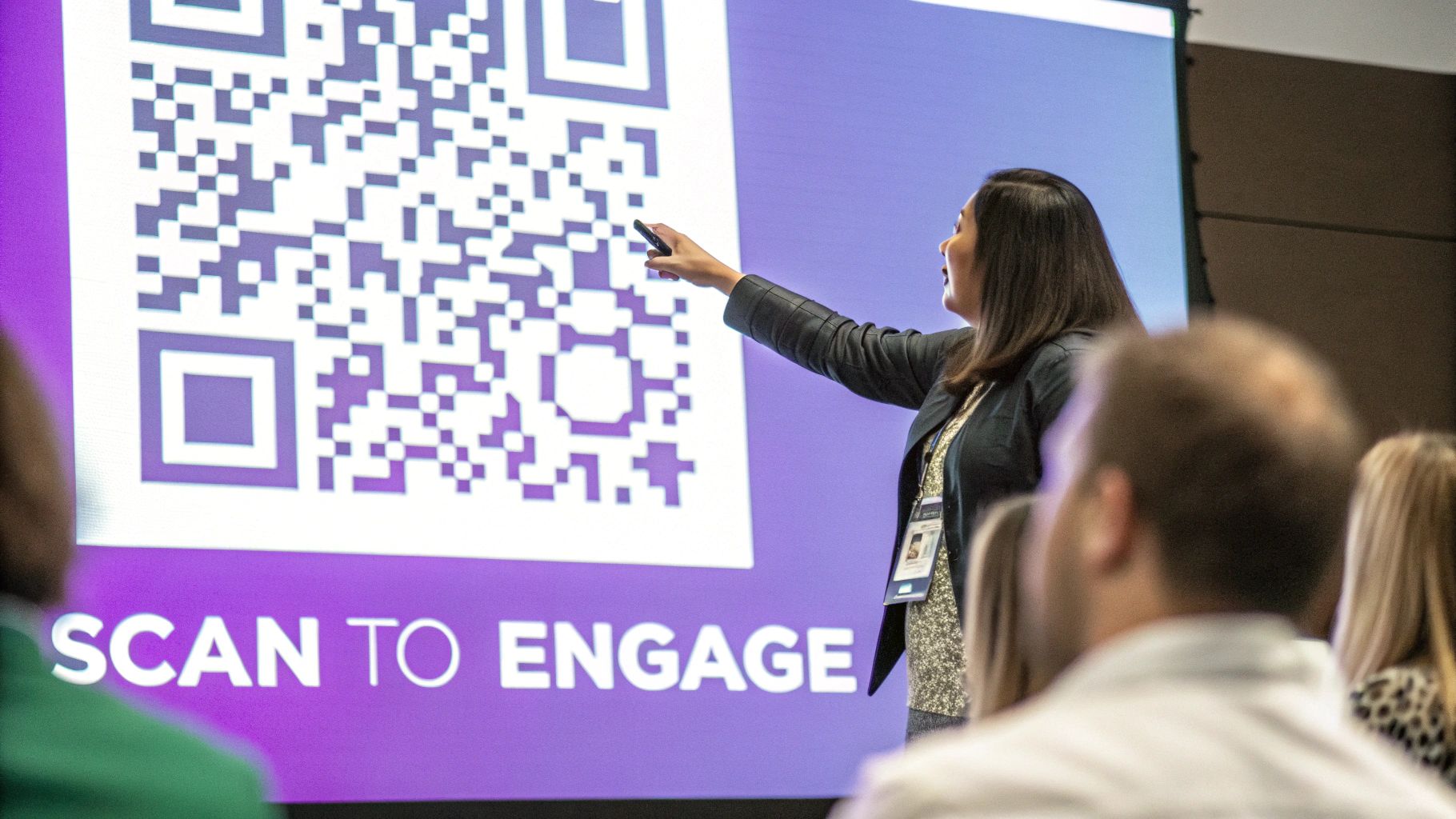 A presenter points to a large QR code on a screen during a conference, encouraging audience engagement.
