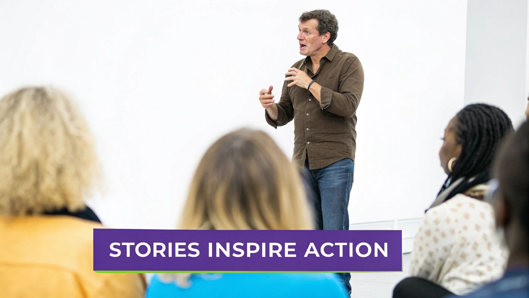 A man in a brown shirt gestures while delivering a keynote speech to an attentive audience, with text 'STORIES INSPIRE ACTION'.
