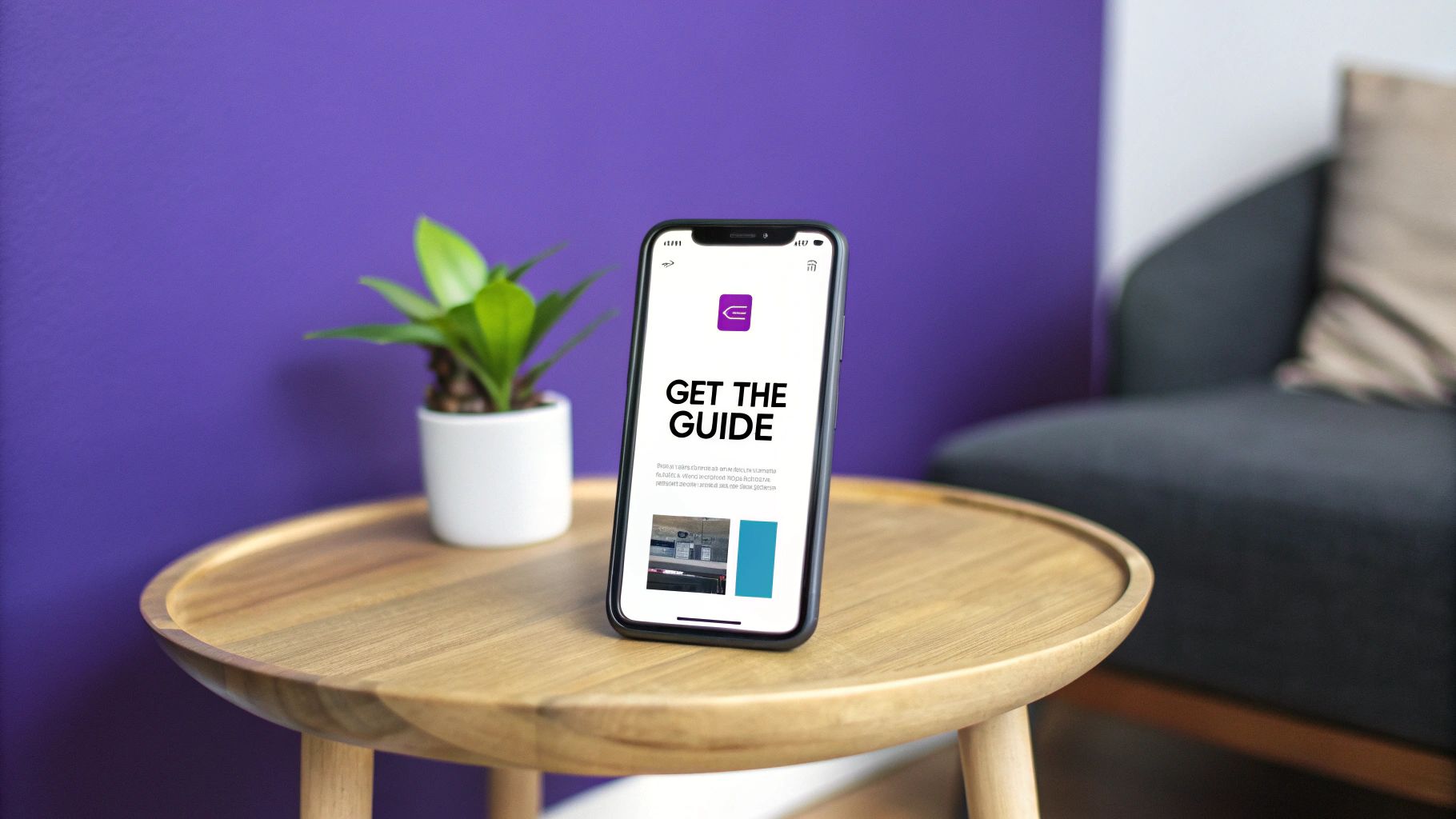 A smartphone displaying 'GET THE GUIDE' on a wooden table with a plant and purple wall background.