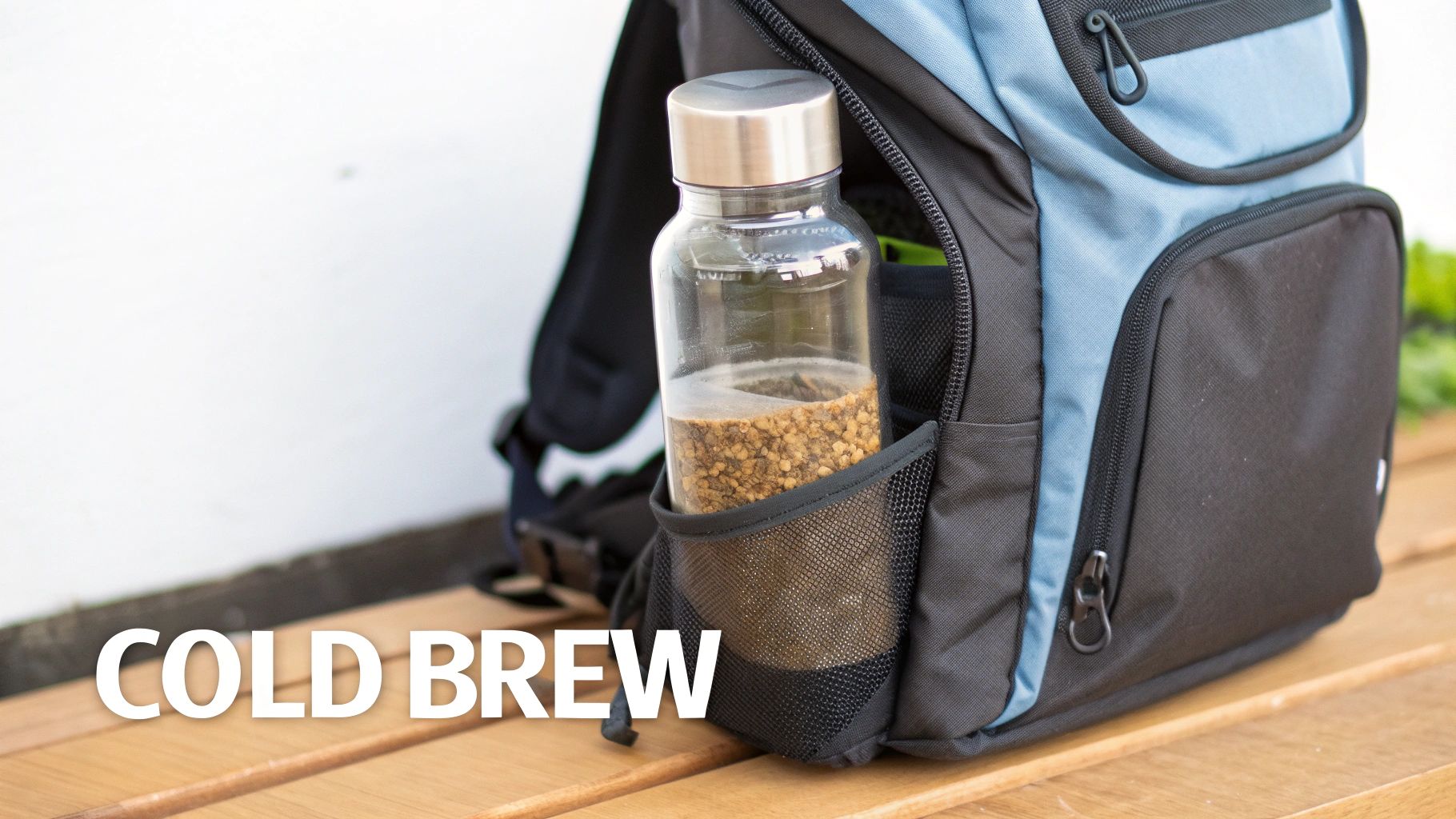 A clear bottle of coffee grounds for cold brew sits in a backpack's mesh side pocket on a wooden bench.