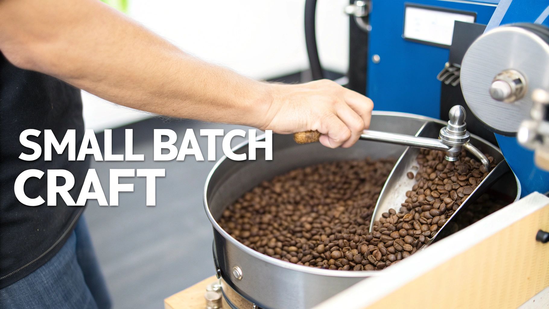 A hand stirs dark roasted coffee beans in a cooling tray, representing small batch craft coffee.