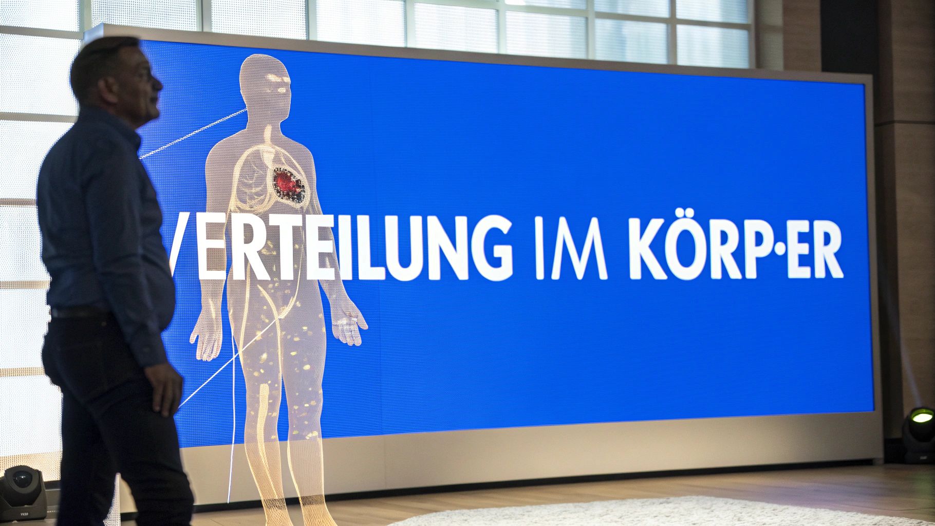 Mann betrachtet einen großen blauen Bildschirm mit einer menschlichen Silhouette und dem Text "Verteilung im Körper".