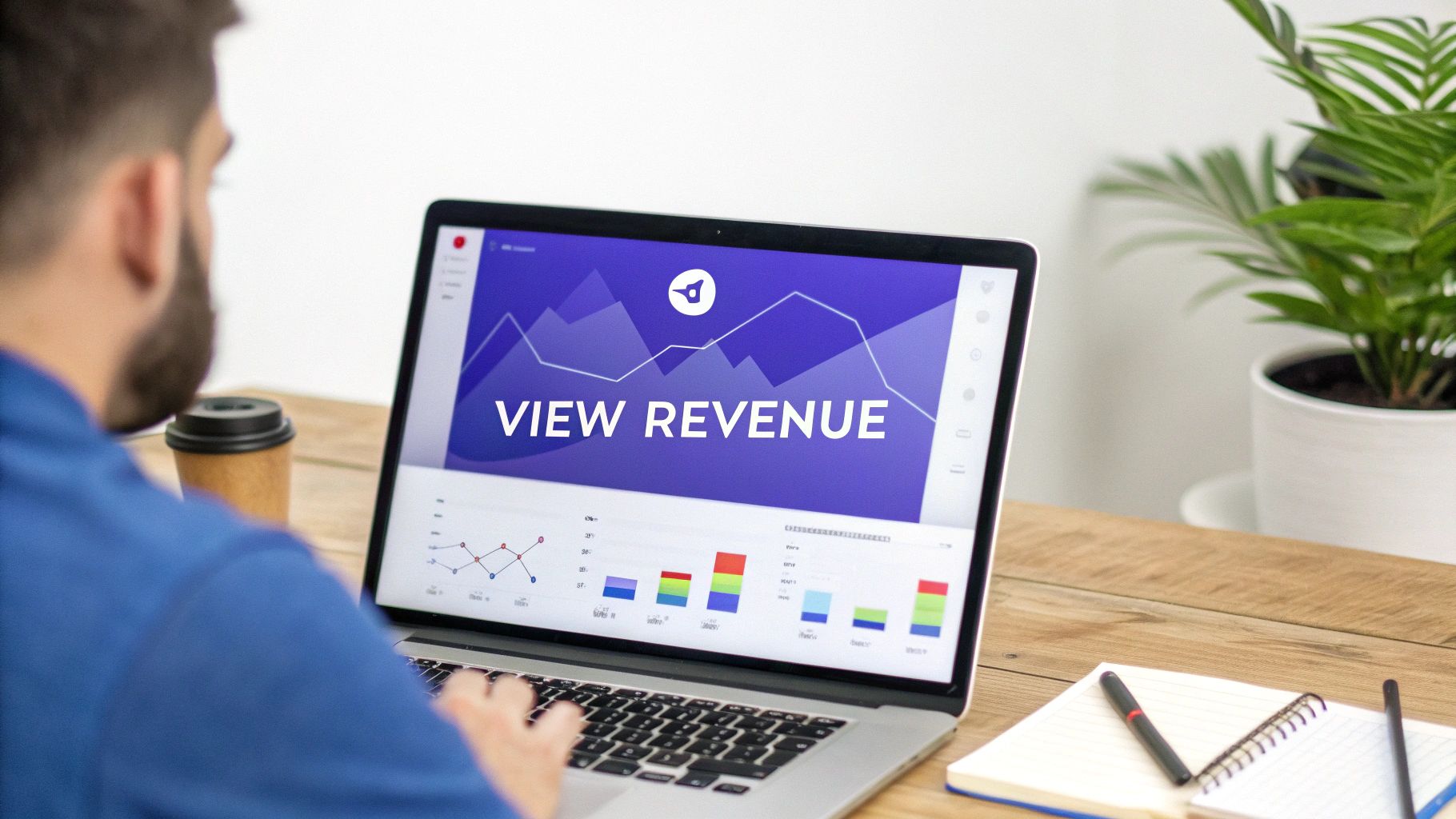 A man views revenue data and graphs on his laptop, with a coffee and notebook on a wooden desk.