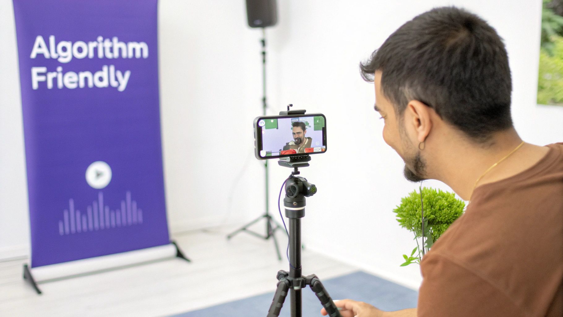A man films himself on a smartphone mounted on a tripod with an 'Algorithm Friendly' banner.