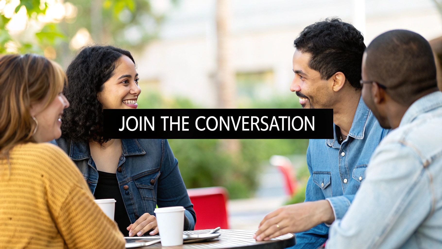 Four diverse people smiling and engaged in conversation at an outdoor table.