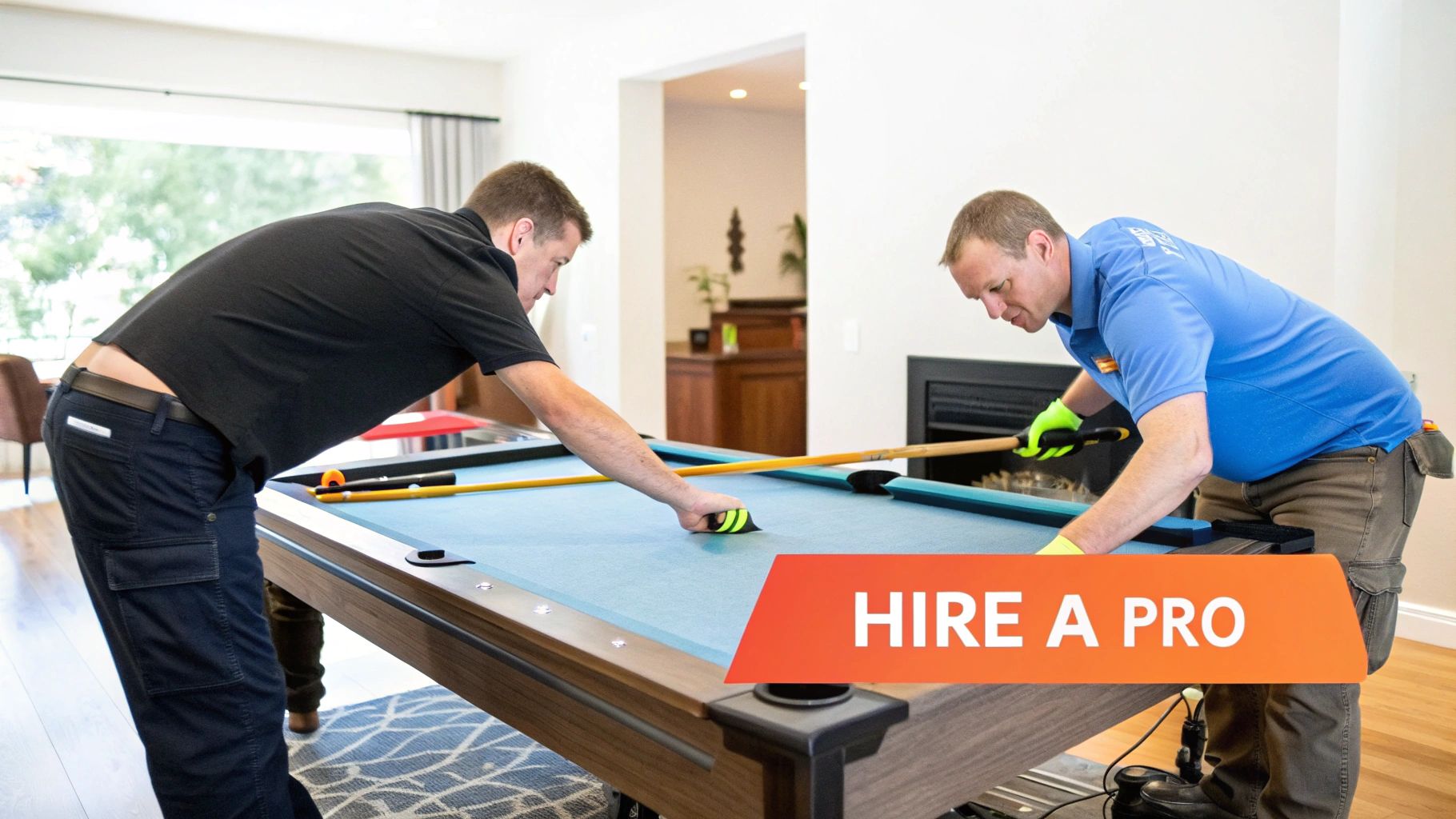 Two professional pool table assemblers working together to stretch and fit the felt onto a slate table, using specialized tools in a well-lit game room.