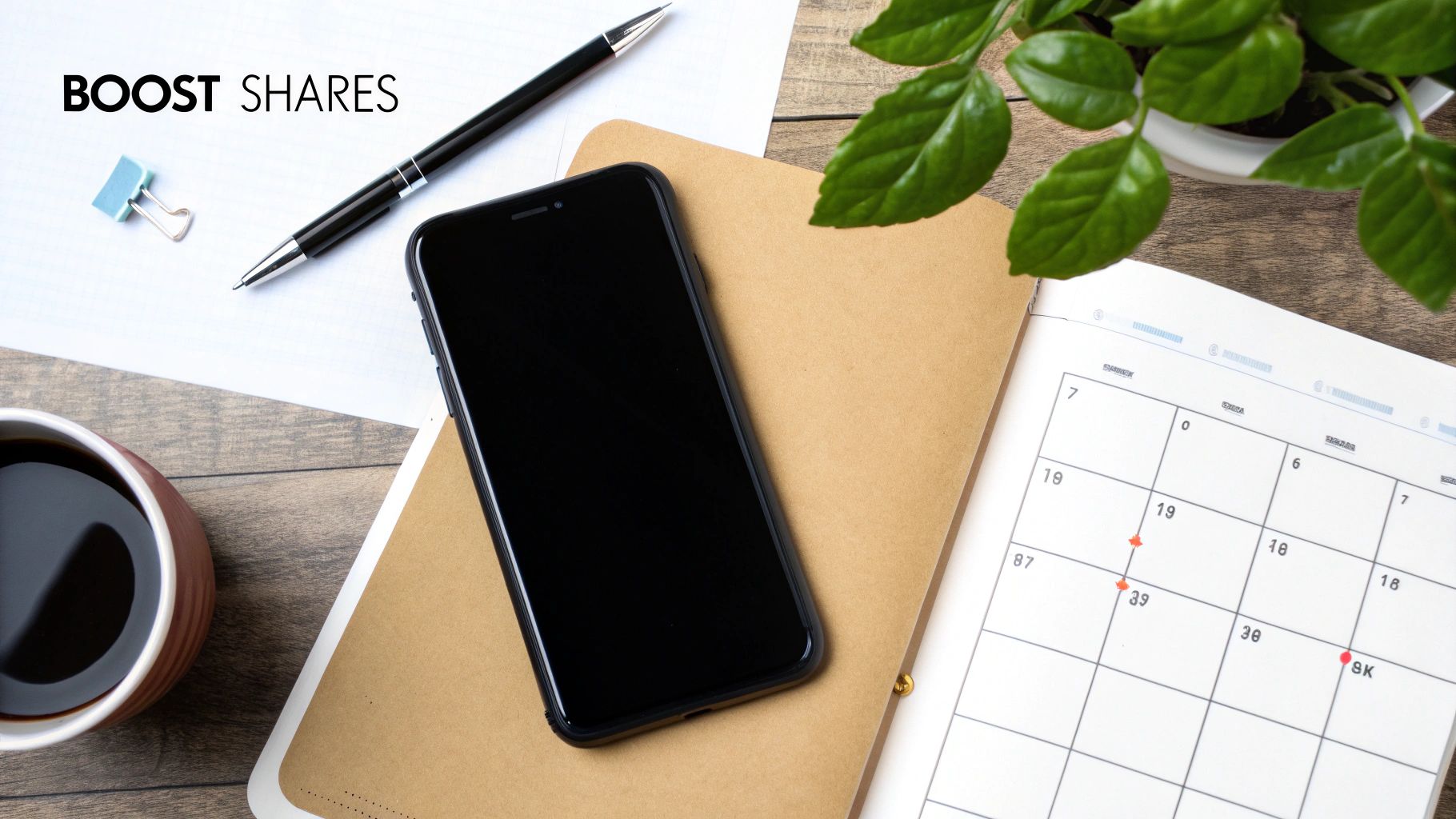Flat lay of a desk with a smartphone, coffee, planner, pen, and 'BOOST SHARES' text.