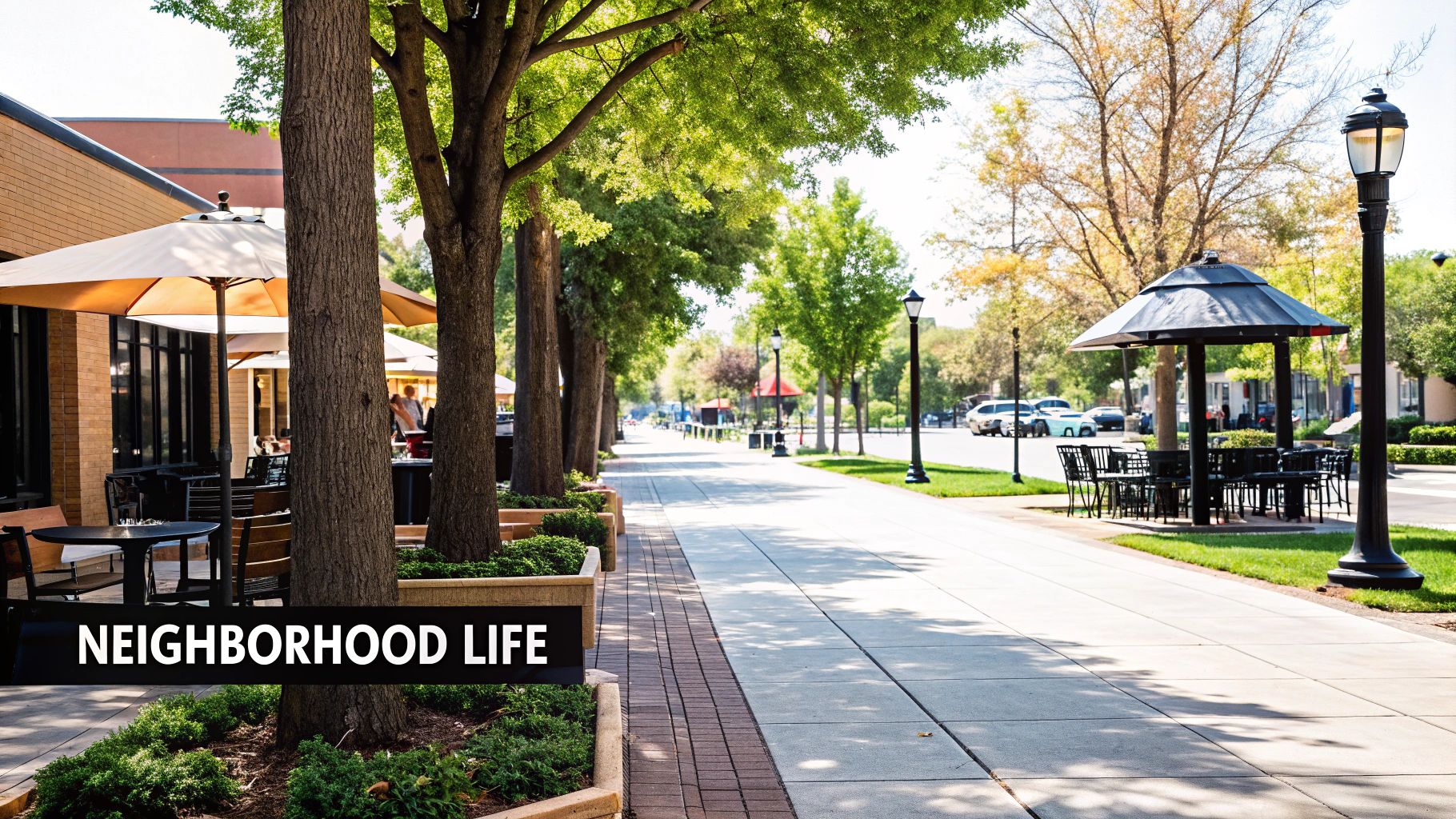 A vibrant neighborhood street with outdoor dining, green trees, a sidewalk, and seating areas.
