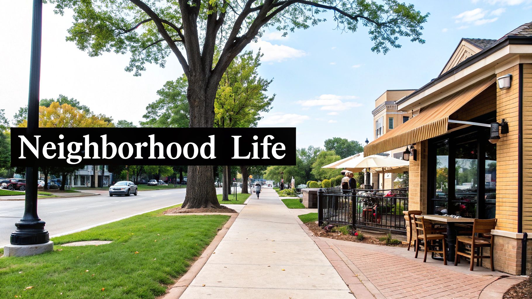 A bustling neighborhood street with a sidewalk, large trees, cars, and an outdoor restaurant patio.