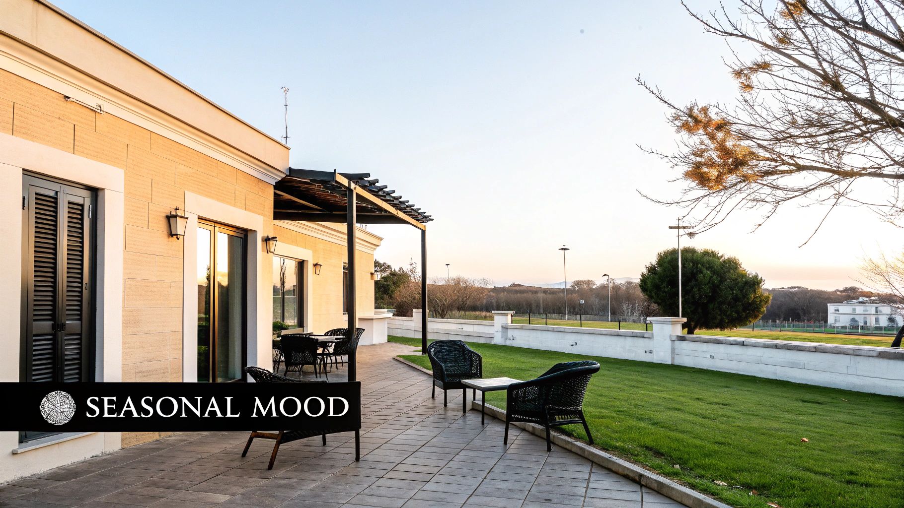 An inviting outdoor terrace with wicker furniture, a green lawn, and distant trees under a bright sky.
