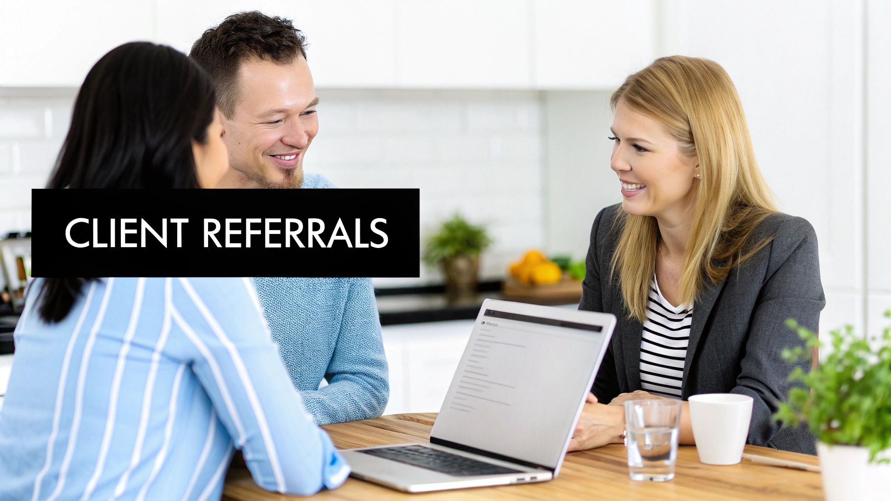 Three smiling professionals, two women and a man, discuss client referrals at a table with a laptop.