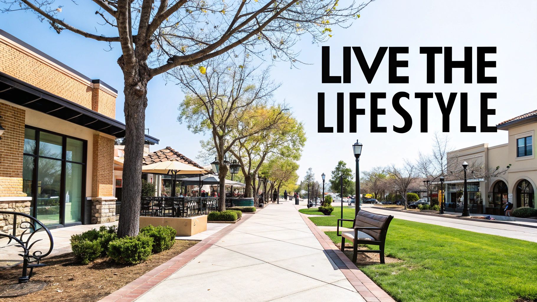 A sunny outdoor shopping center with brick buildings, trees, a sidewalk, and outdoor seating.
