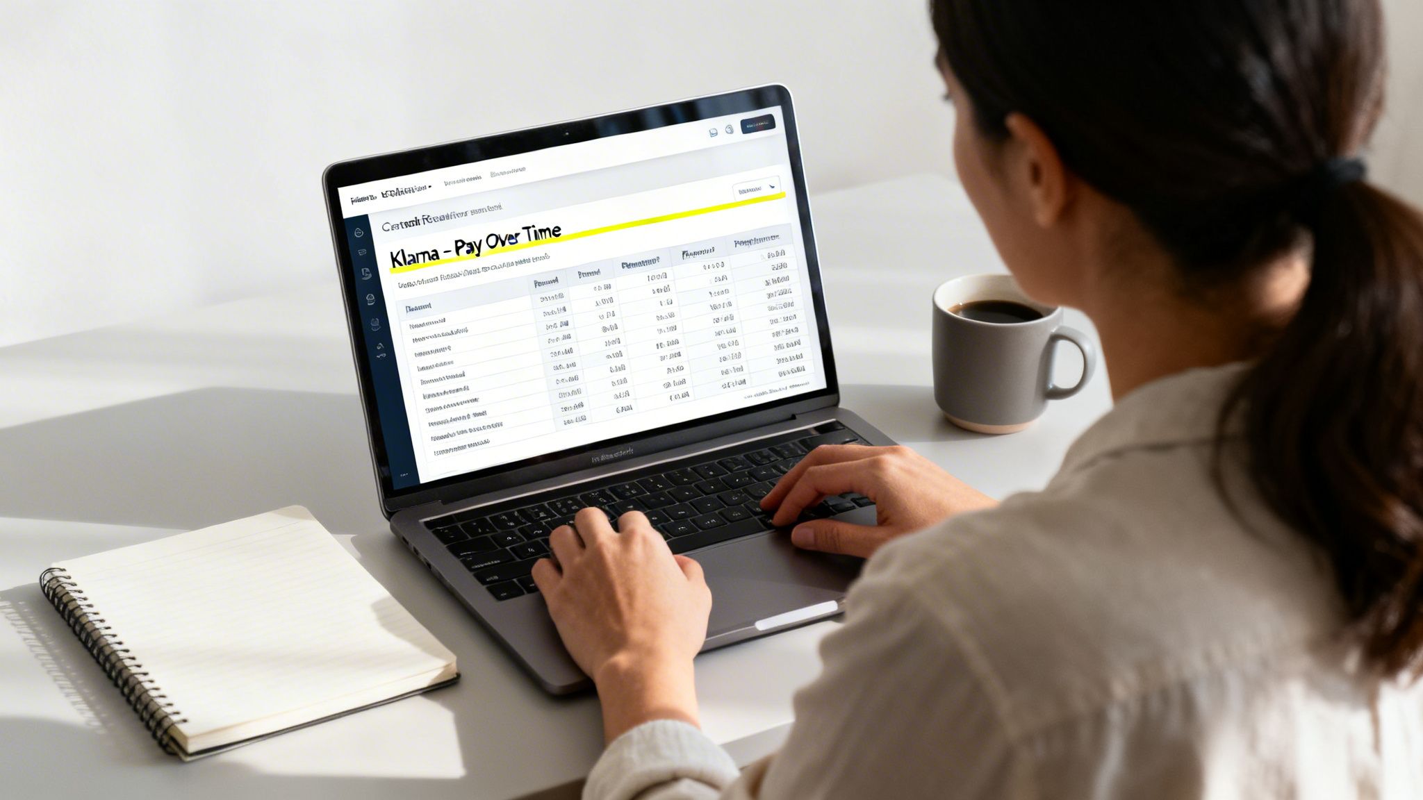 Person typing on a laptop displaying a Klarna 'Pay Over Time' screen, with coffee and a notebook on the desk.