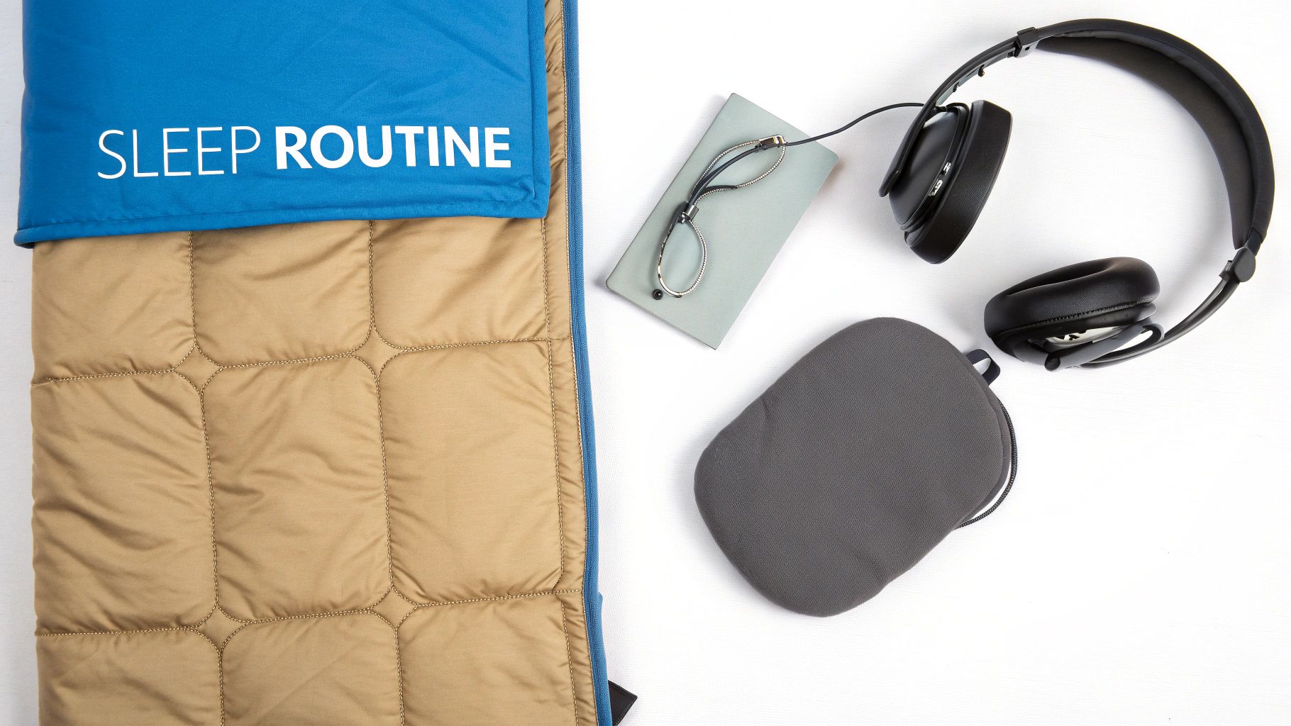 A flat lay showing sleep routine essentials: a sleeping bag, headphones, a notebook, and reading glasses.