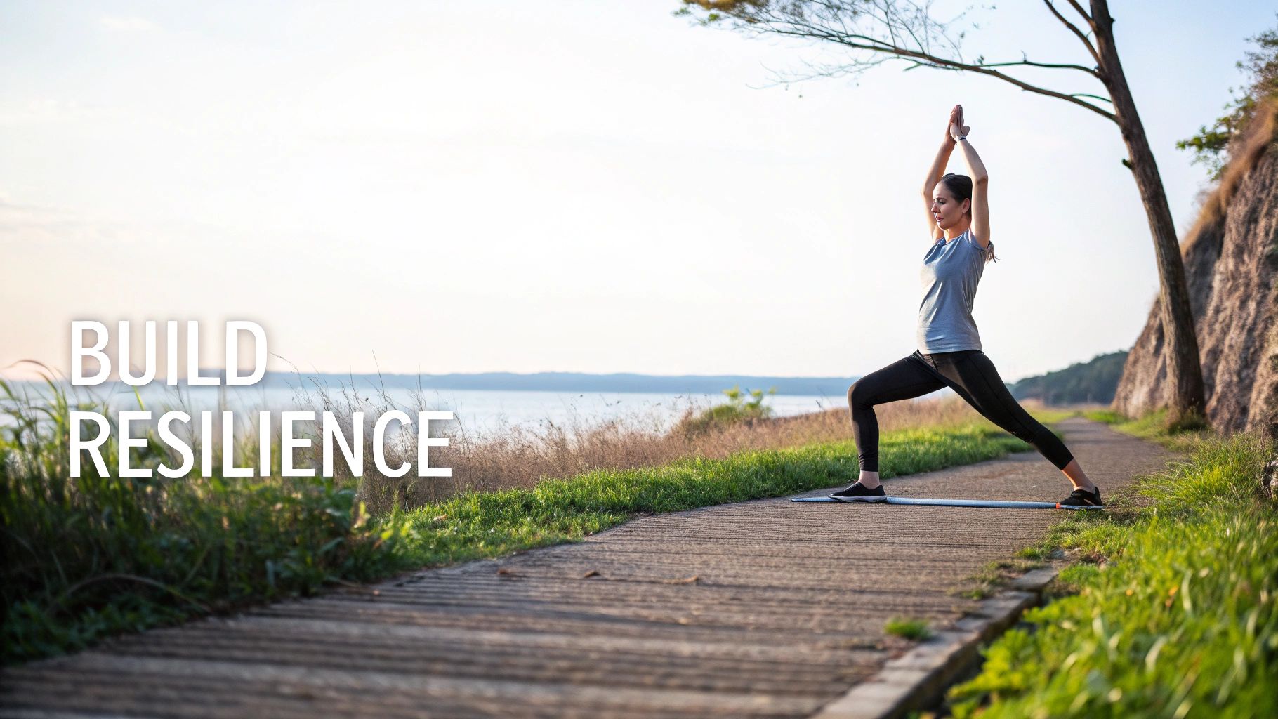 Woman practicing yoga warrior pose outdoors on path by water to build resilience and calm nervous system