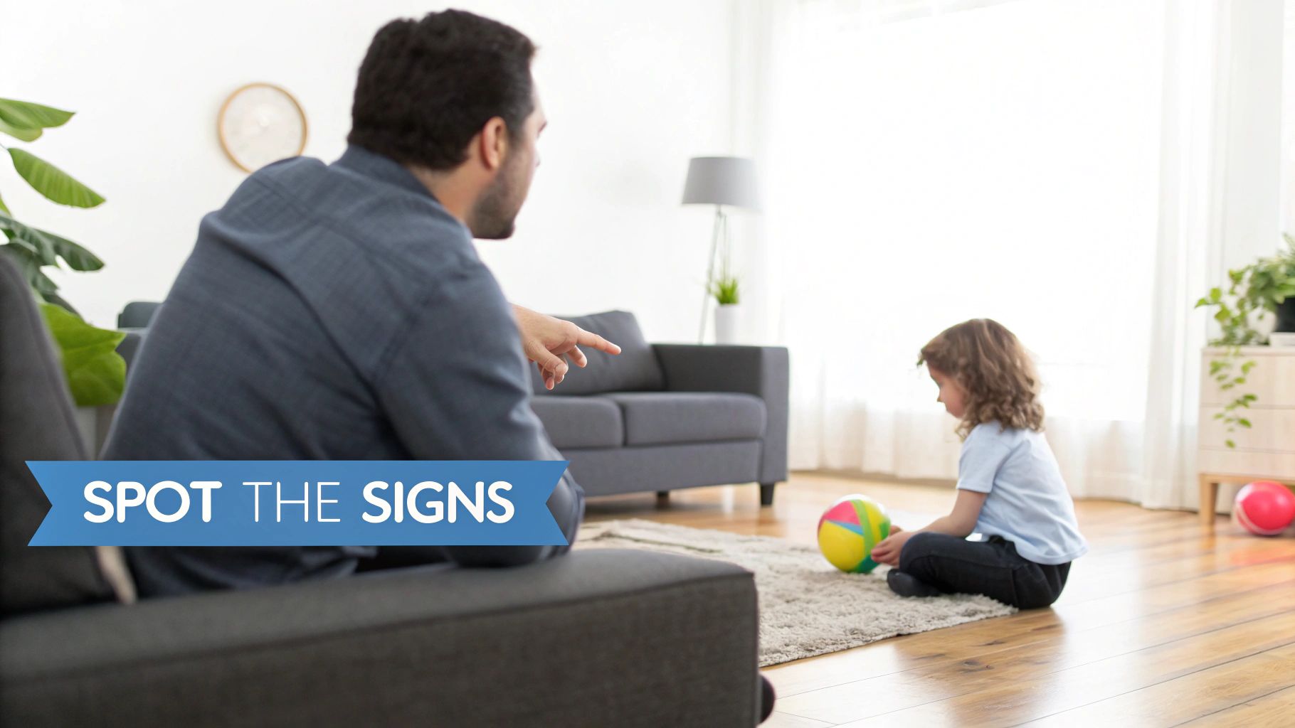 An adult points at a child playing with a colorful ball on a rug in a bright living room.
