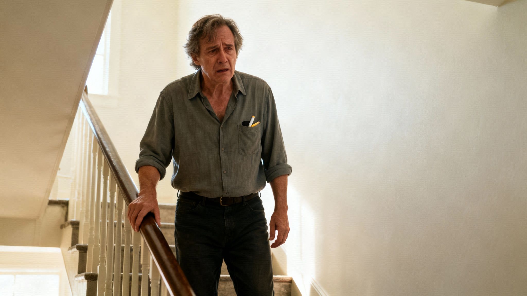 Un homme âgé au visage préoccupé, avec deux cigarettes dans sa poche, descend un escalier.