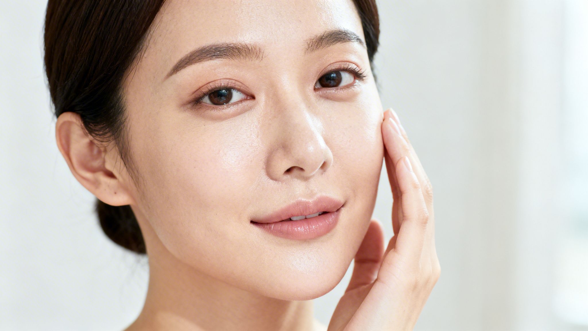 A beautiful East Asian woman with clear, healthy skin gently touching her cheek.
