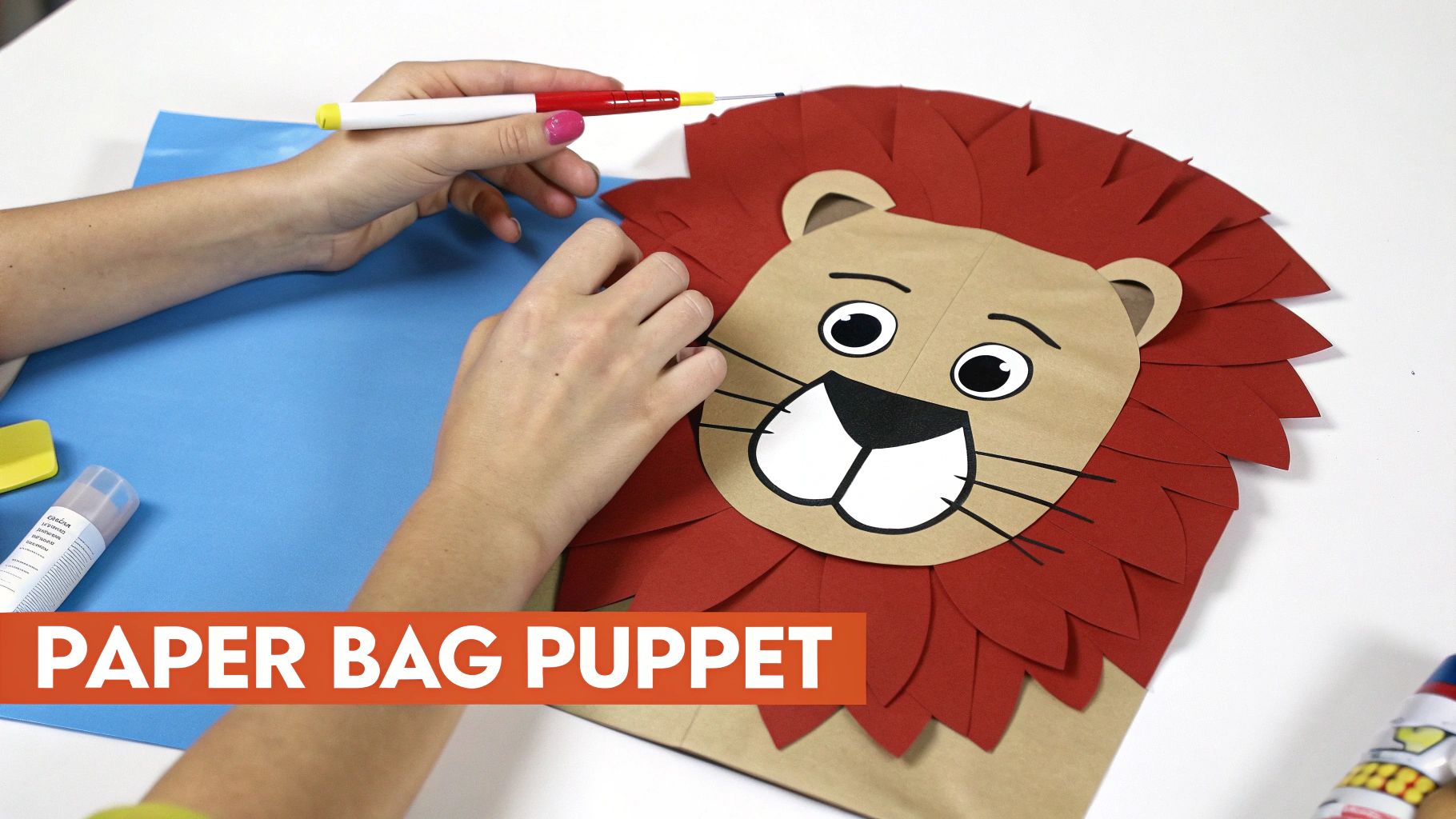 Hands crafting a lion paper bag puppet with a red mane, blue paper, and crafting tools.