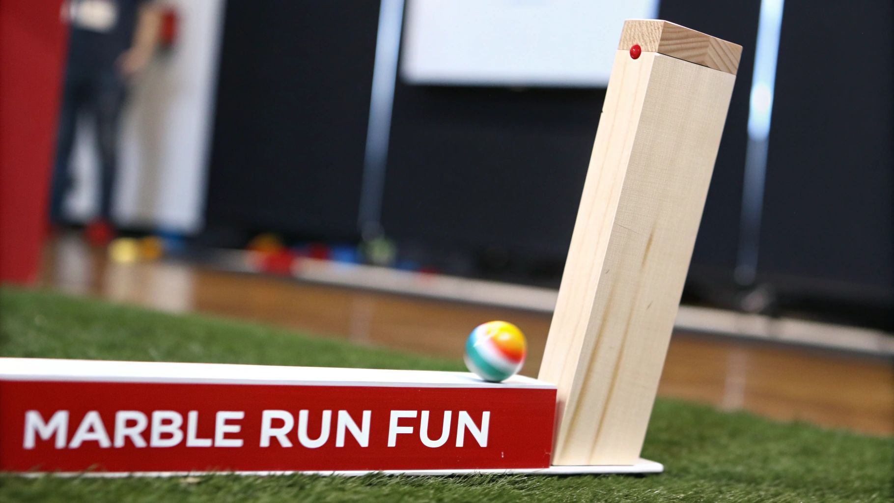 A colorful marble rests on a "MARBLE RUN FUN" track made of wood and a red base, set on green turf.