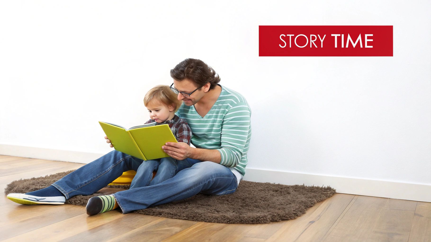 A father and his toddler son sitting on a rug, joyfully reading a green storybook together.