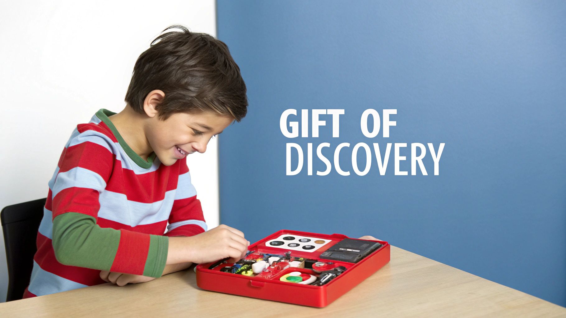 A happy young boy engaged and smiling while playing with a red science kit, 'Gift of Discovery'.