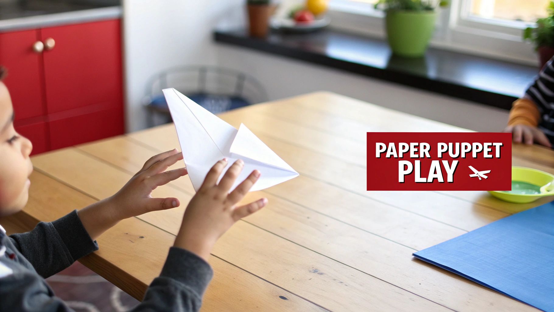 A young child's hands are holding a white paper airplane on a wooden table, ready for play.