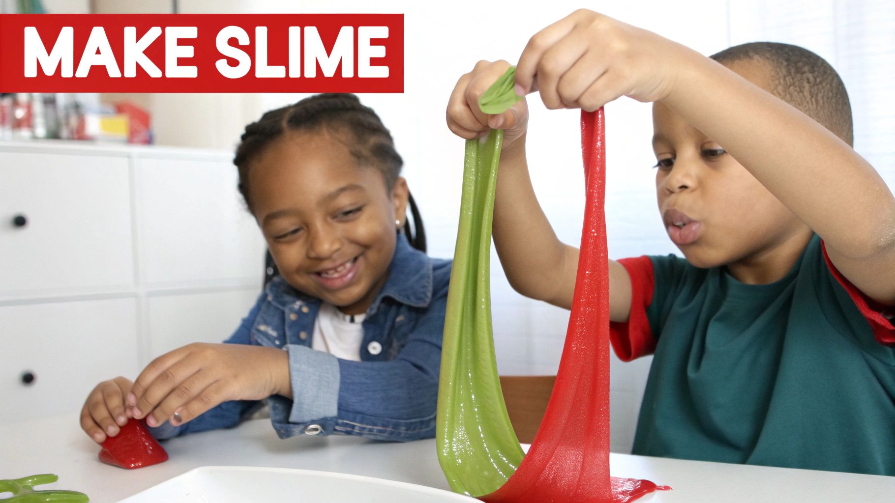 Two happy children playing with colorful green and red slime at a table, enjoying a fun activity.